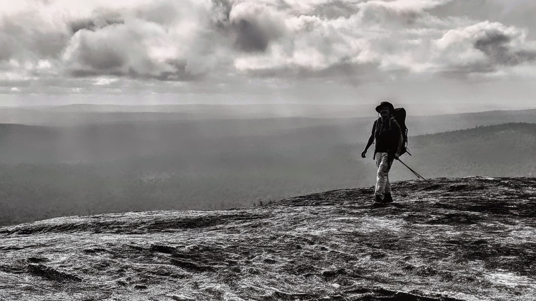 black and white photo of man hiking with big backpack on granite rock