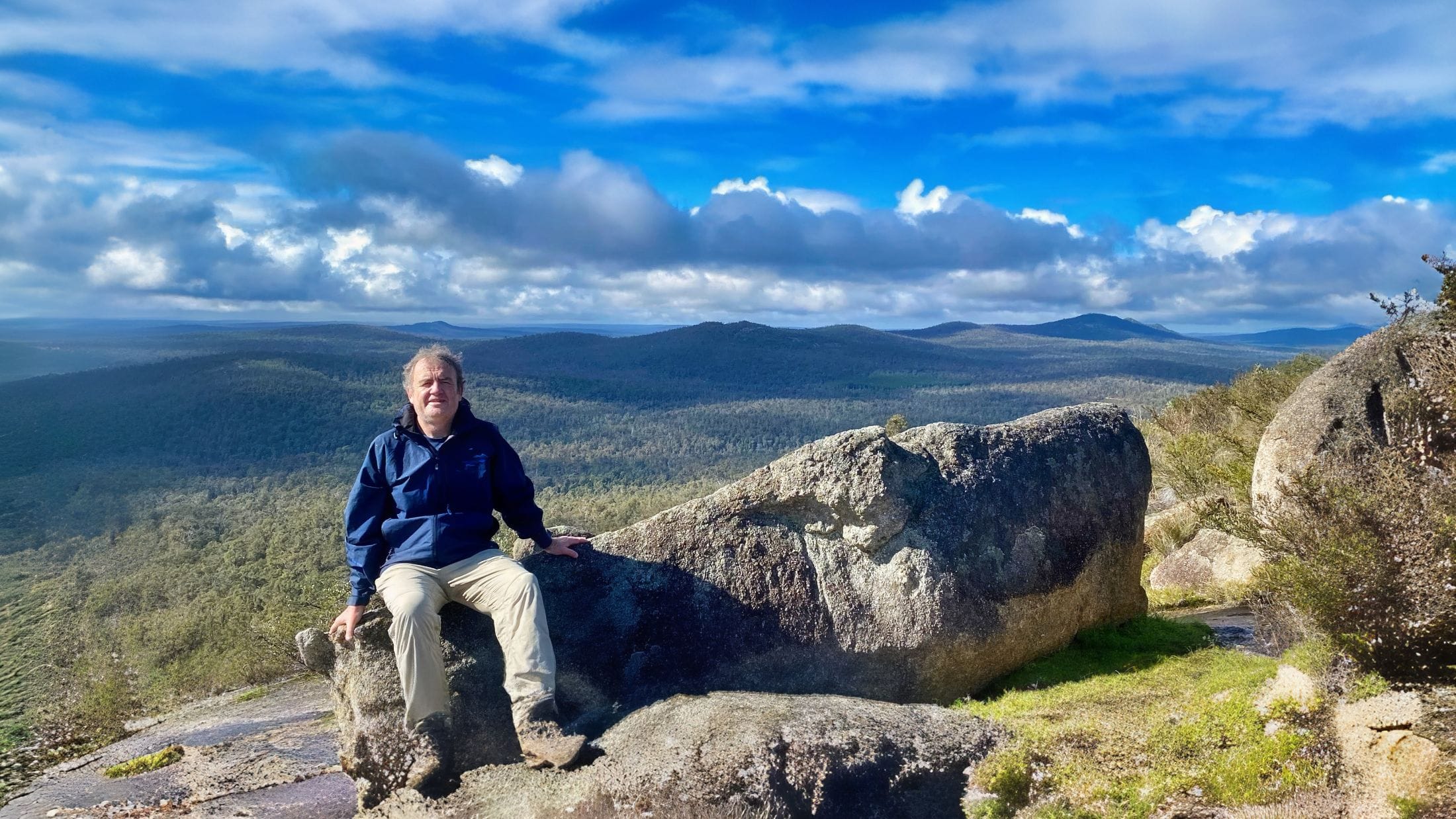 man sitting on a rock on mt cuthbert down to forrest behind him