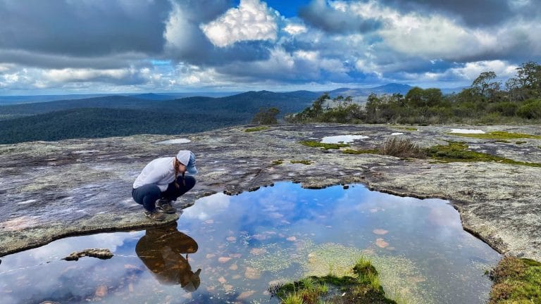 young lady hiker looking in mountain puddle