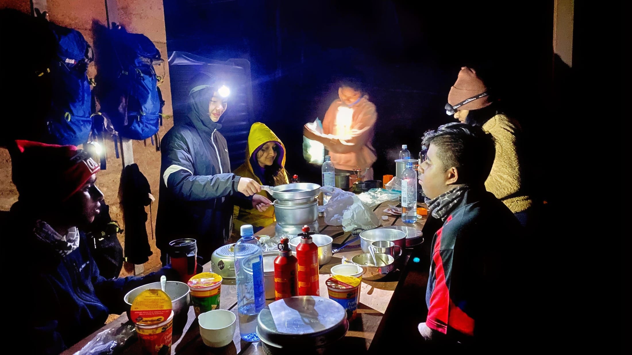 Teen hikers wearing headlamps while preparing an evening meal at a campsite shelter