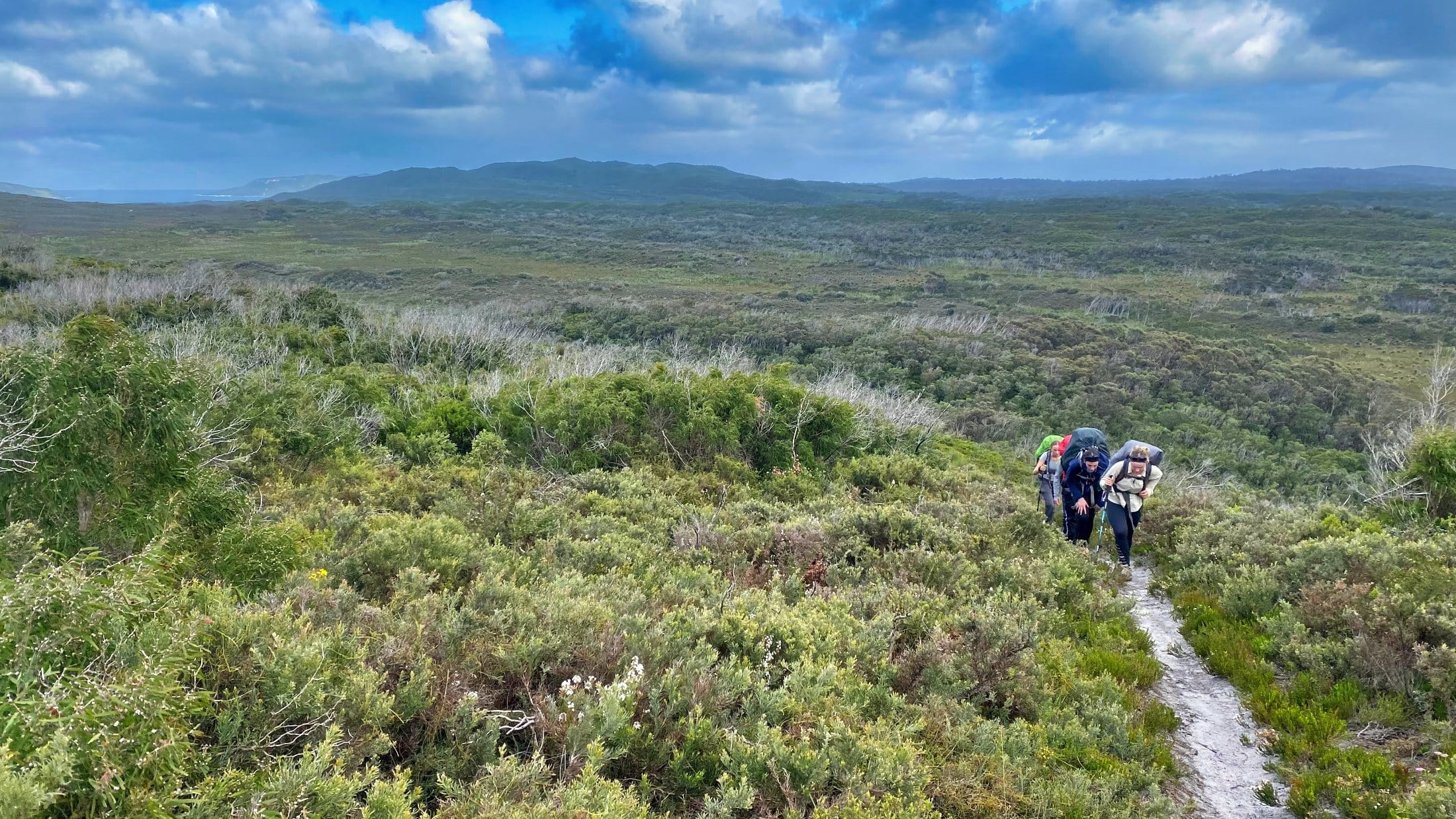 teens hiking up a hill with big packs