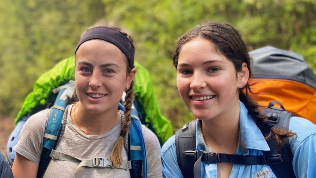 two smiling teen girls during a 7 day hike carrying their large backpacks